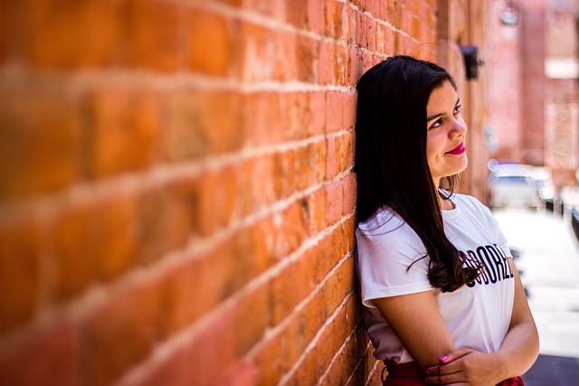 Woman leaning against a brick wall, thinking.