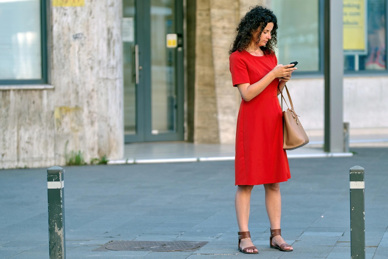 woman in red dress on sidewalk looking at smartphone
